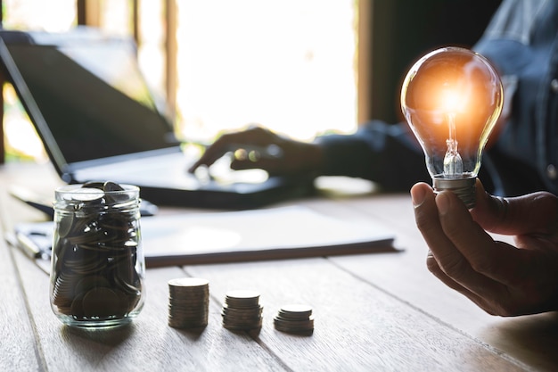 Hand des Mannes eine Glühlampe mit Stapel Münzen halten