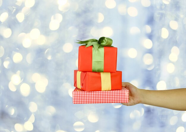 Hand des Mannes mit einer roten Weihnachtsgeschenkbox auf grauem bokeh Hintergrund.