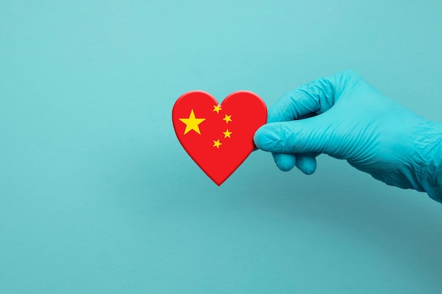 Hand des medizinischen Personals, das einen chirurgischen Handschuh trägt, der das Herz der chinesischen Flagge hält