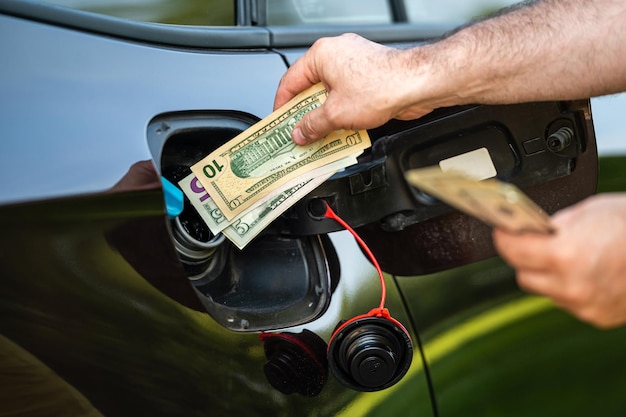 Hand des Menschen, die Geld in den Tank des Autos steckt, Nahaufnahme des Konzepts der teuren Kraftstoffkrise