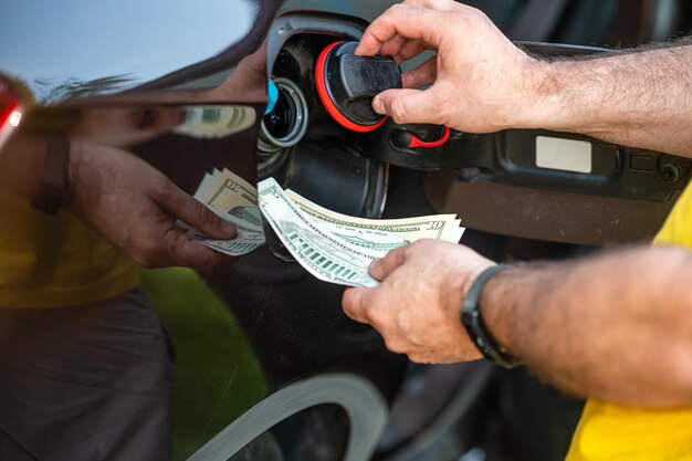 Hand des Menschen, die Geld in den Tank des Autos steckt, Nahaufnahme des Konzepts der teuren Kraftstoffkrise