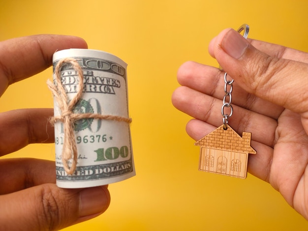 Hand, die Banknoten und Hausschlüsselbund auf gelbem Hintergrund hält