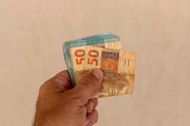 Hand, die beige Hintergrund des brasilianischen Geldes hält