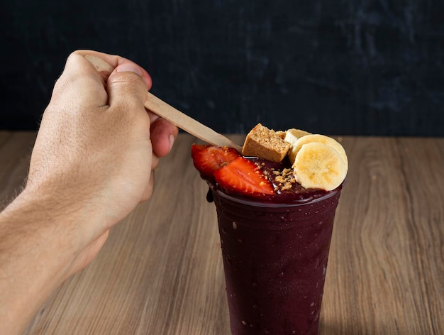 Hand, die brasilianische Acai-Beere mit Erdbeere, Banane und Pacoca hält.