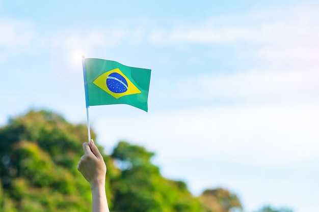 Hand, die Brasilien-Flagge auf Hintergrund des blauen Himmels hält. Unabhängigkeitstag im September und fröhliche Feierkonzepte