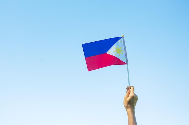 Hand, die die philippinische Flagge auf Naturhintergrund hält 12. Juni des Unabhängigkeitstages und fröhliche Feierkonzepte