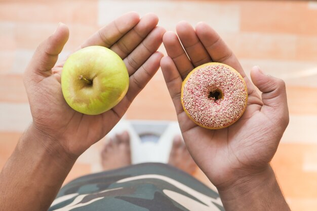 Hand, die Donuts und Apfel auf der Waage zur Hand hält.