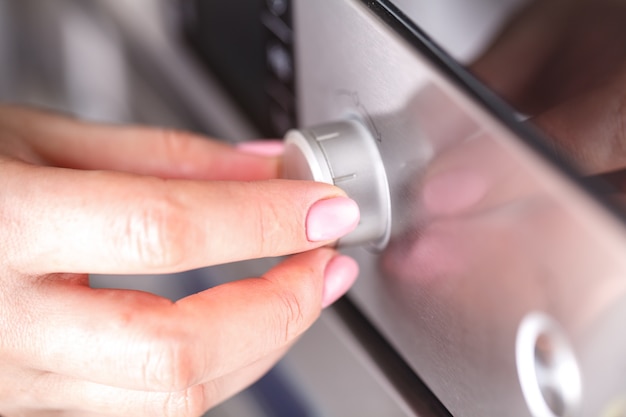 Hand, die Drehkreisknopfwärme des Mikrowellenofens für das Kochen von Lebensmitteln im Küchenraum zu Hause, Nahaufnahme hält.