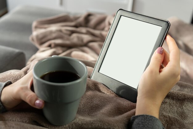 Hand, die ein eBook mit einer Tasse Kaffee im Vordergrund unscharf hält