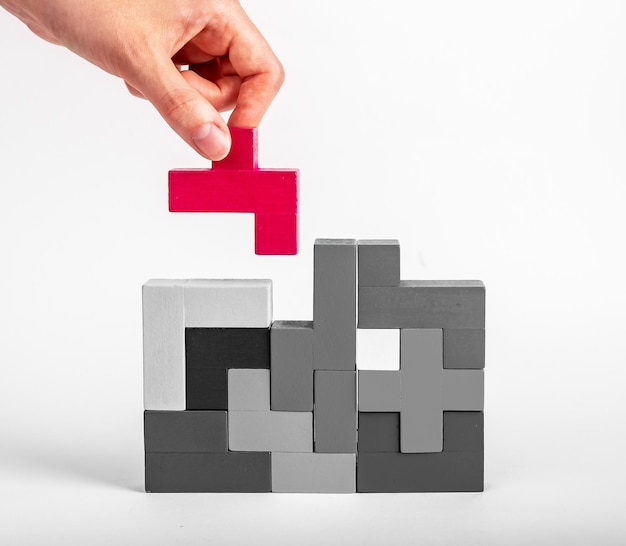 Hand, die ein herausragendes rotes Element in die Tetris-Puzzle-Konstruktion einfügt und nach einem geeigneten Ort für Details sucht Konstruktionsbildungskonzept Gute Idee