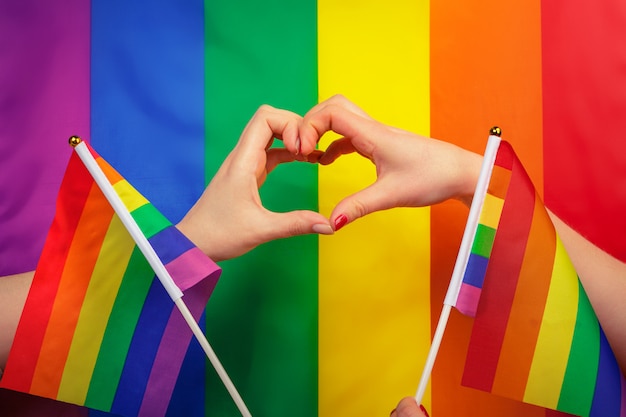 Hand, die ein Herzzeichen mit LGBT-Regenbogenflagge des homosexuellen Stolzes macht