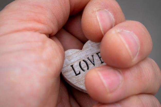 Foto hand, die ein holzherz mit dem schriftzug liebeszeichen der liebe in der hand hält