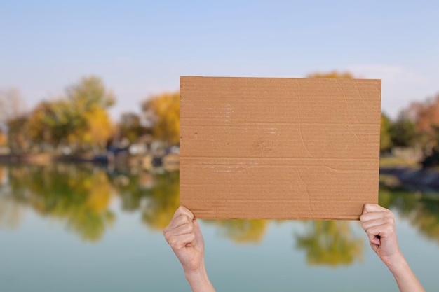 Hand, die ein leeres Pappschild vor verschwommenem Seehintergrund hält