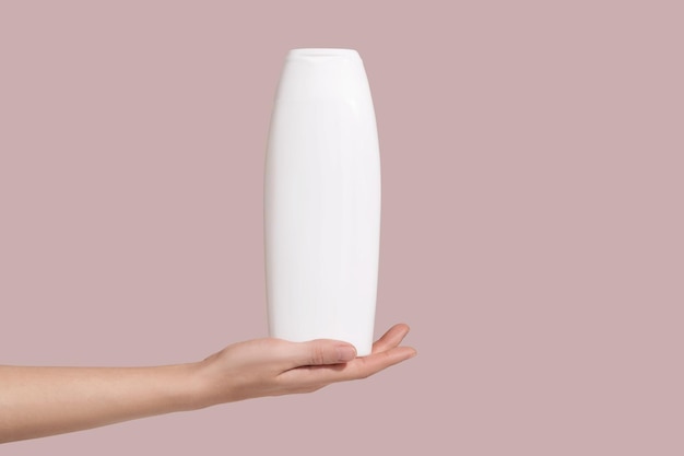 Hand, die ein leeres weißes Kunststoffrohr auf rosa Hintergrund hält Branding-Mockup für kosmetische Schönheitsprodukte