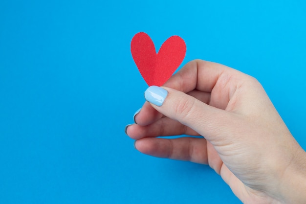 Hand, die ein rotes Herz auf einem blauen Hintergrund hält. Hintergrund für den Valentinstag