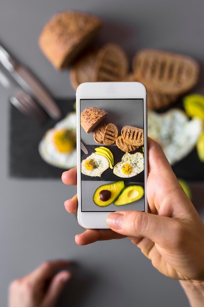 Hand, die ein Smartphone-Foto vom Frühstück mit Avocados und Eiern macht