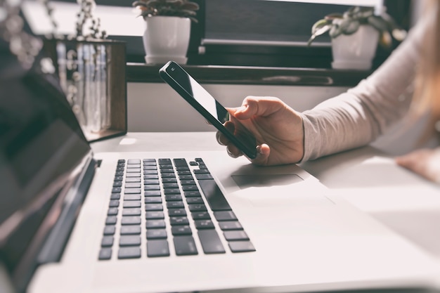 Hand, die ein Smartphone nahe Laptop hält