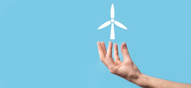 Hand, die ein Symbol einer Windmühle hält, die Umweltenergie auf blauem Hintergrund erzeugt.