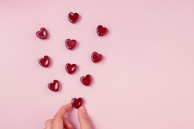 Hand, die eine der verstreuten roten Gelee-Bonbons der Herzform, Draufsicht hält. Valentinstag Komposition