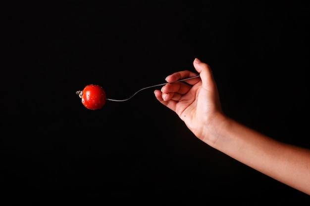 Hand, die eine Gabel mit einer roten reifen Tomate hält