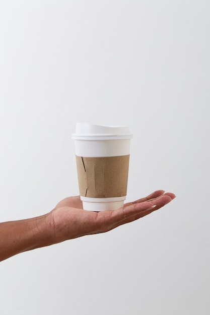 Hand, die eine Kaffeepapiertasse lokalisiert auf hellgrauer Wand hält