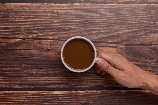 Hand, die eine Kaffeetasse auf einem hölzernen Hintergrund hält