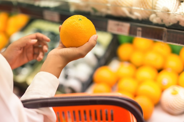 Hand, die eine Orange in einem Supermarkt hält