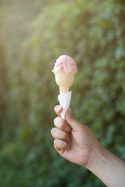 Hand, die eine rosa Eiscreme hält. Sommer warmes Bild