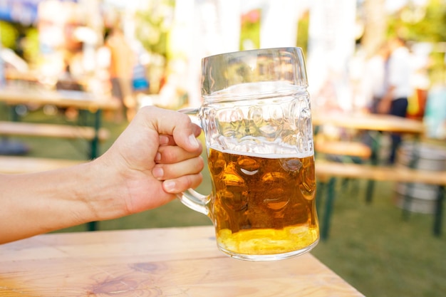 Hand, die einen Becher Bier hält, der das Oktoberfest röstet