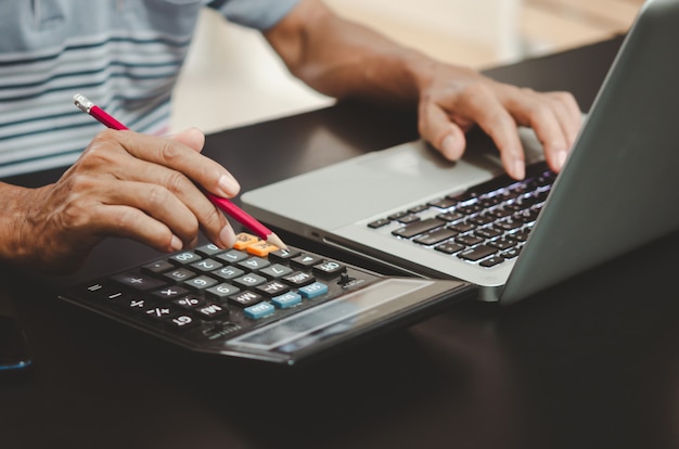 Hand, die einen Bleistift, einen Taschenrechner und eine Computertastatur auf dem Schreibtisch hält.