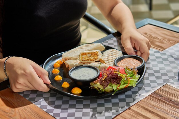 Hand, die einen frischen Tortilla-Wrap hält, der mit braunem Papier und Schnur umgebunden ist. Gourmet-Konzeption.