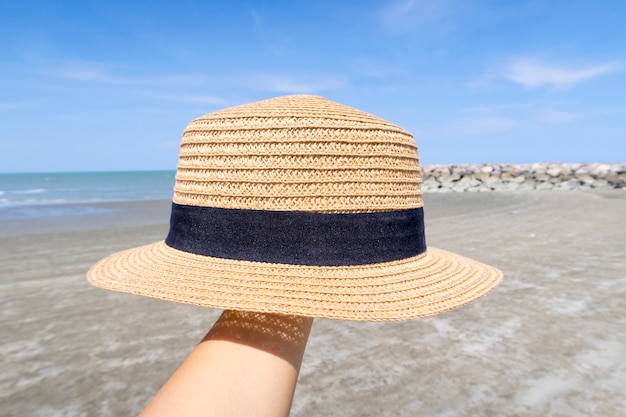 Hand, die einen Hut mit Strandhintergrund hält