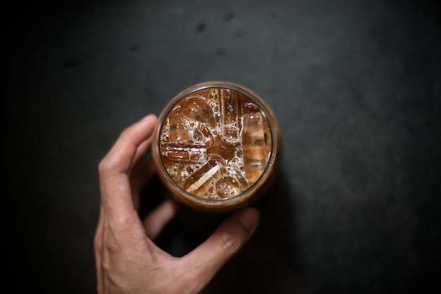 Hand, die einen Kaffee zum Mitnehmen auf einem schwarzen Tisch hält