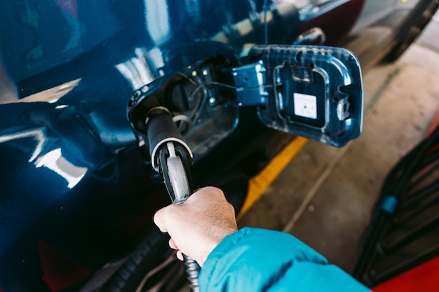 Hand, die einen Schlauch hält, der an einer Tankstelle in einem metallblauen Auto an ein Auto aus LPG-Kraftstoff (Flüssiggas) angeschlossen ist. Tanken, Tankstelle, Ökologie, Transport und Ökokonzept.