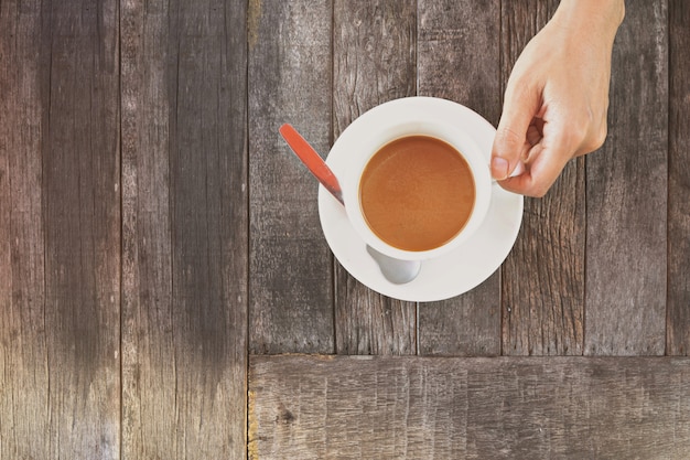 Hand, die einen Tasse Kaffee auf Holztisch hält.