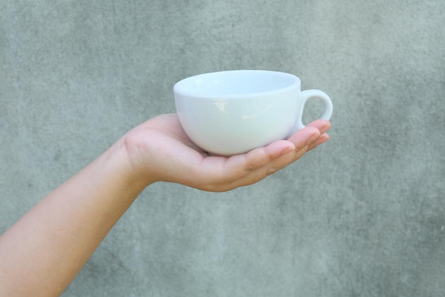 Hand, die einen Tasse Kaffee auf Wandhintergrund hält