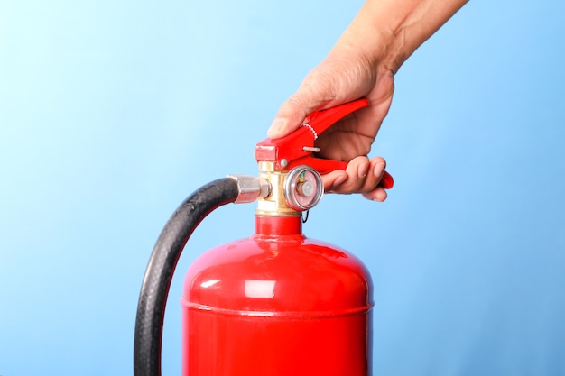 Hand, die Feuerlöscher auf blauem Hintergrund hält.