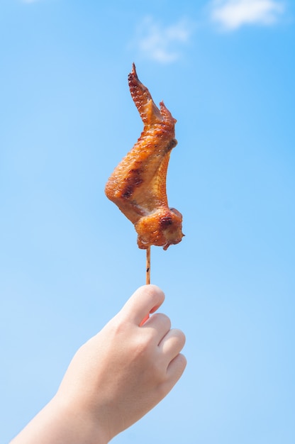 Hand, die gegrillte Hühnerflügel auf blauem Himmel hält