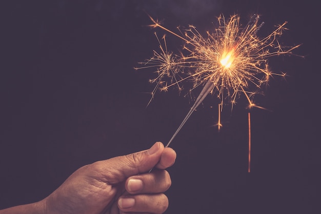 Hand, die hellen brennenden Weihnachtsschein auf Schwarzem hält