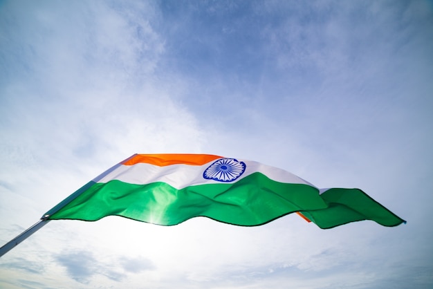 Hand, die Indien-Flagge auf dem Hintergrund des blauen Himmels hält.