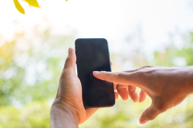 Hand, die intelligentes Telefon auf Naturhintergrund hält