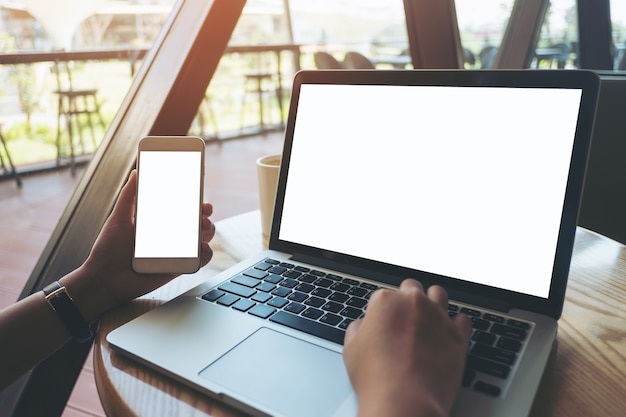 Hand, die intelligentes Telefon des Modells mit Laptop hält