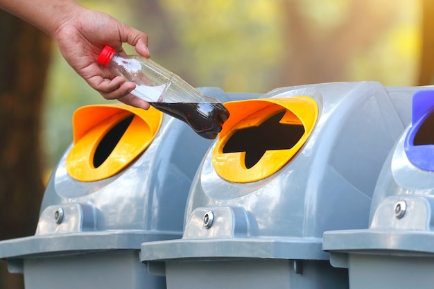 Hand, die leere Plastikwasserflasche in den Wiederverwertungsbehälter wirft