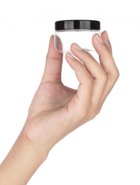 Hand, die leere transparente runde Plastikkosmetik lokalisiert auf weißem Hintergrund hält.
