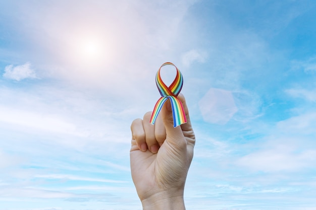 Hand, die LGBTQ-Regenbogenband gegen Himmelhintergrund am Morgen zeigt.