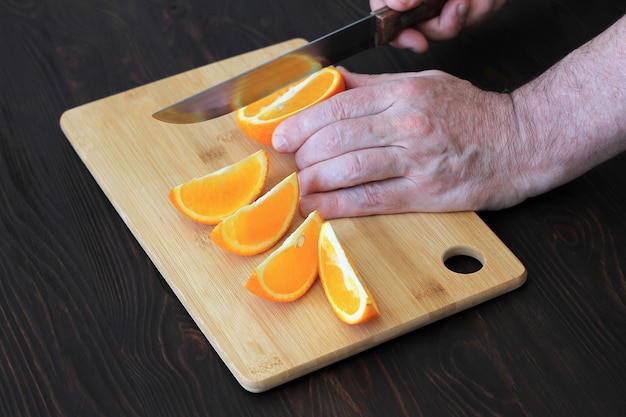 Hand, die Orange auf hölzernem Brett schneidet