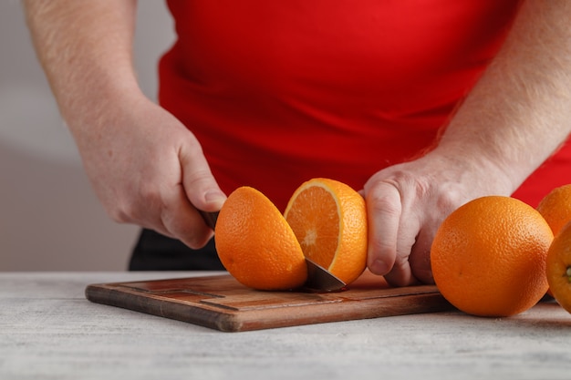 Hand, die Orange auf Holzbrett schneidet