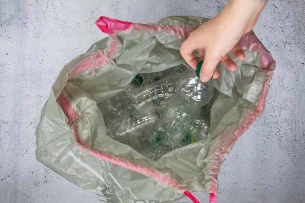 Hand, die Plastikflaschen in Müllsäcken entsorgt, die bereit sind, die Abfallwirtschaft zu recyceln