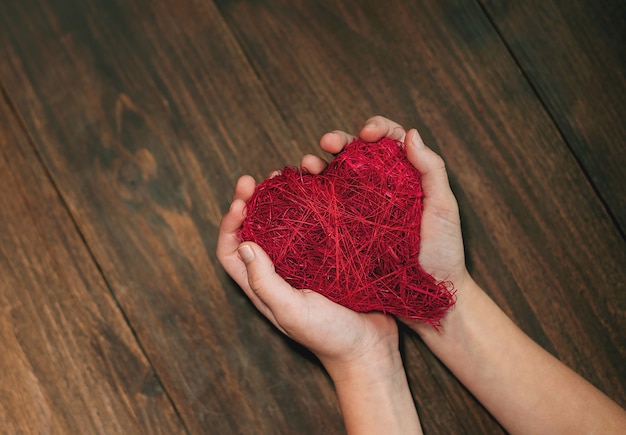 Hand, die rotes Herz auf Holzhintergrund hält