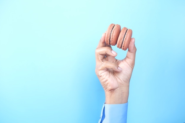 Hand, die Schokoladenmakrone gegen blauen Hintergrund hält